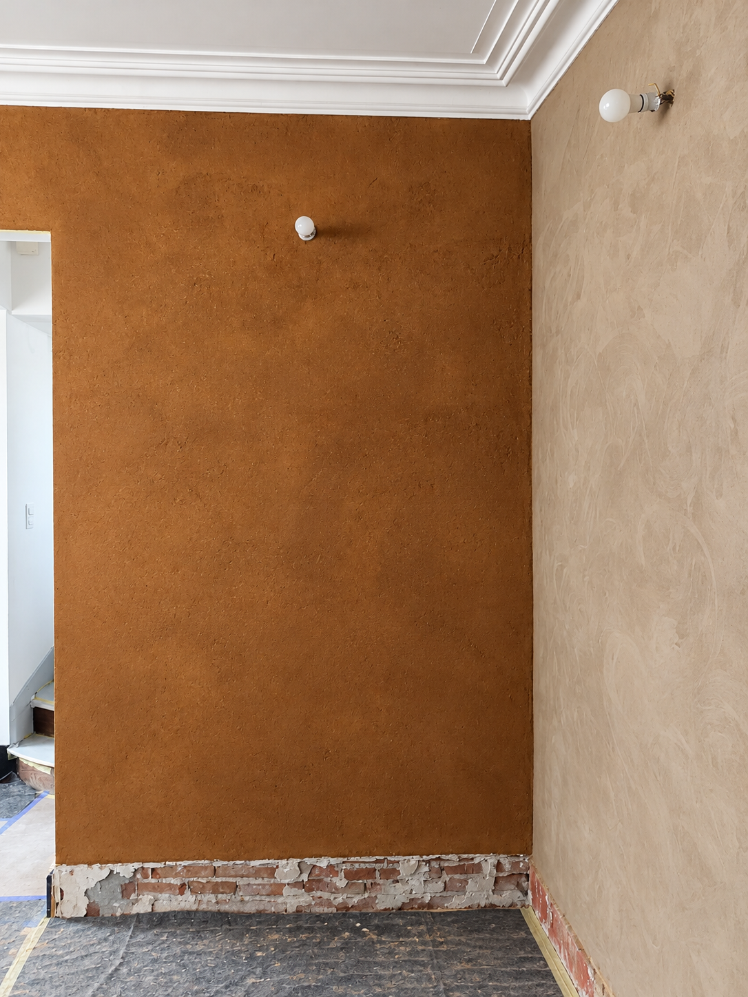 Enduit décoratif en terre aux teintes ocres et brun chaud, avec une texture verticale en relief sur les murs d'une pièce en rénovation.